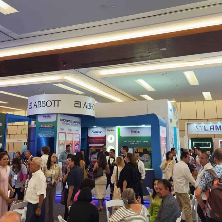 Stand de Abbott en evento de salud con muchas personas interactuando y exhibiciones de productos médicos.