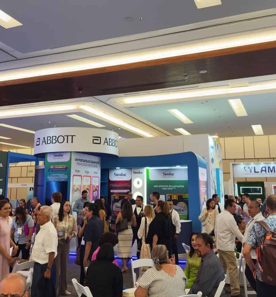 Stand de Abbott en evento de salud con muchas personas interactuando y exhibiciones de productos médicos.