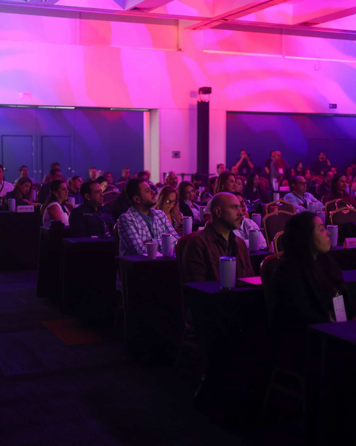 Asistentes en conferencia en León Guanajuato, participando en evento con iluminación vibrante y ambiente profesional.