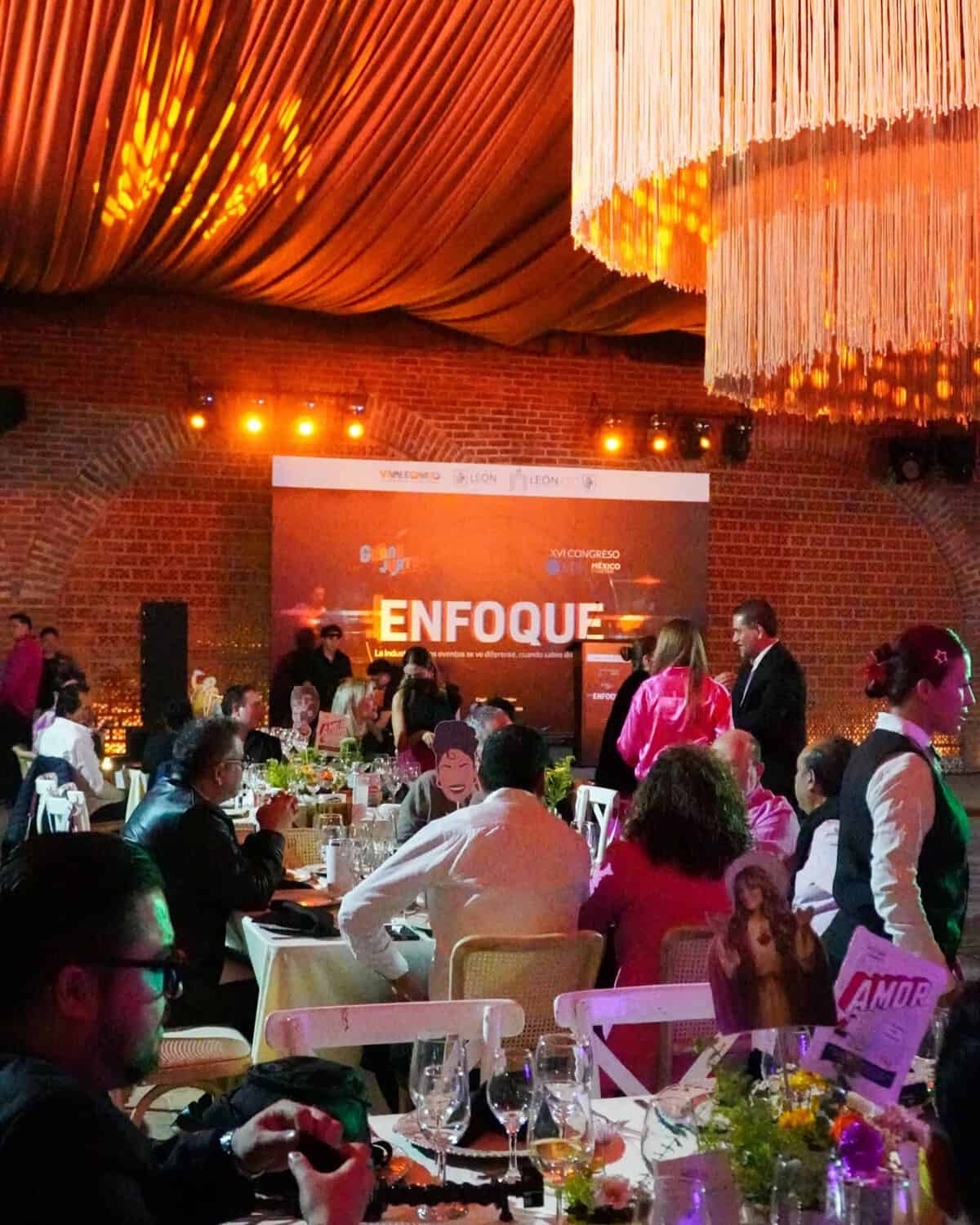 Conferencia en León, Guanajuato con asistentes y escenario iluminado, evento cultural y empresarial en un espacio moderno.