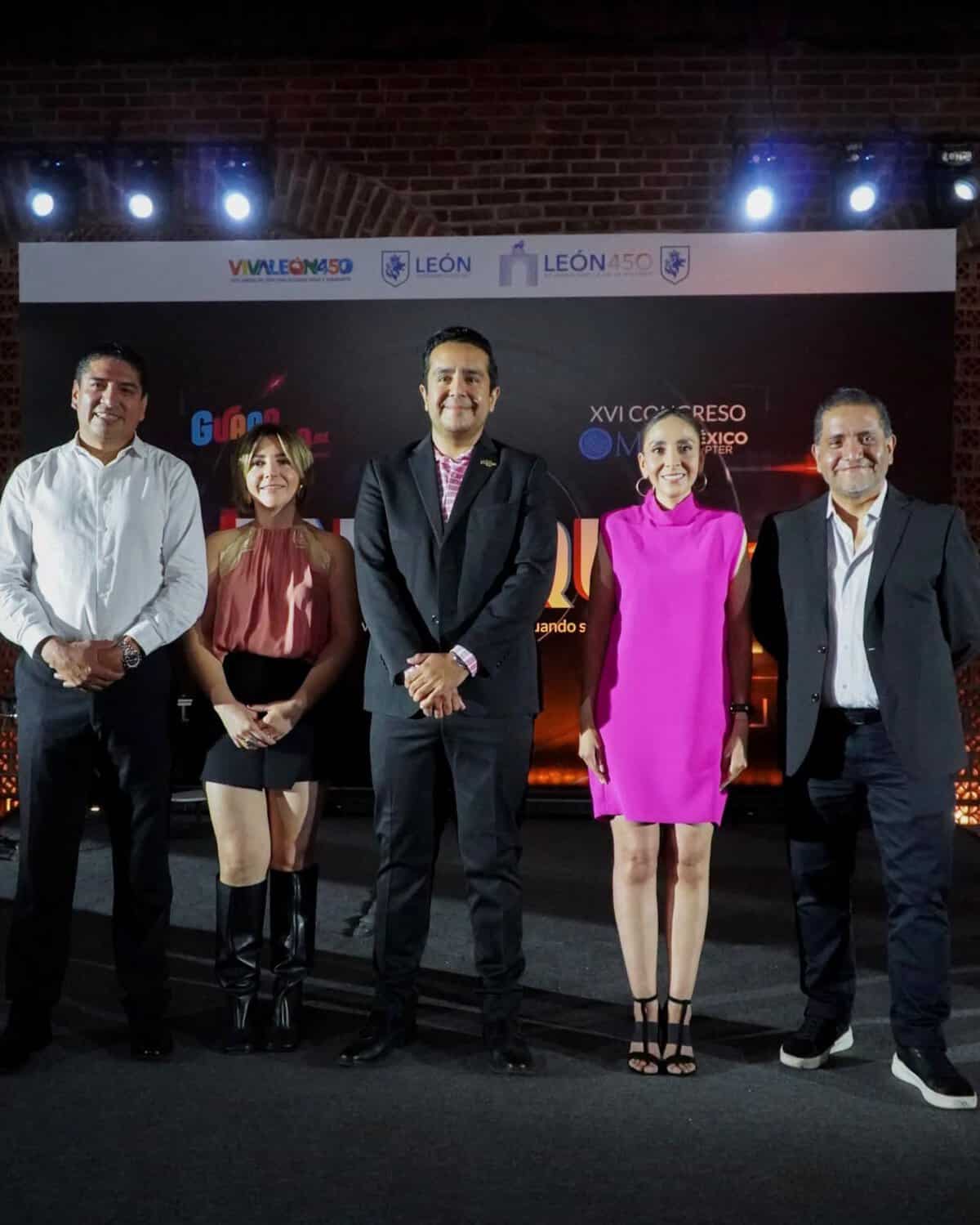 Grupo de cinco personas en escenario durante evento en León, Guanajuato, México, con fondo de pantalla y luces.