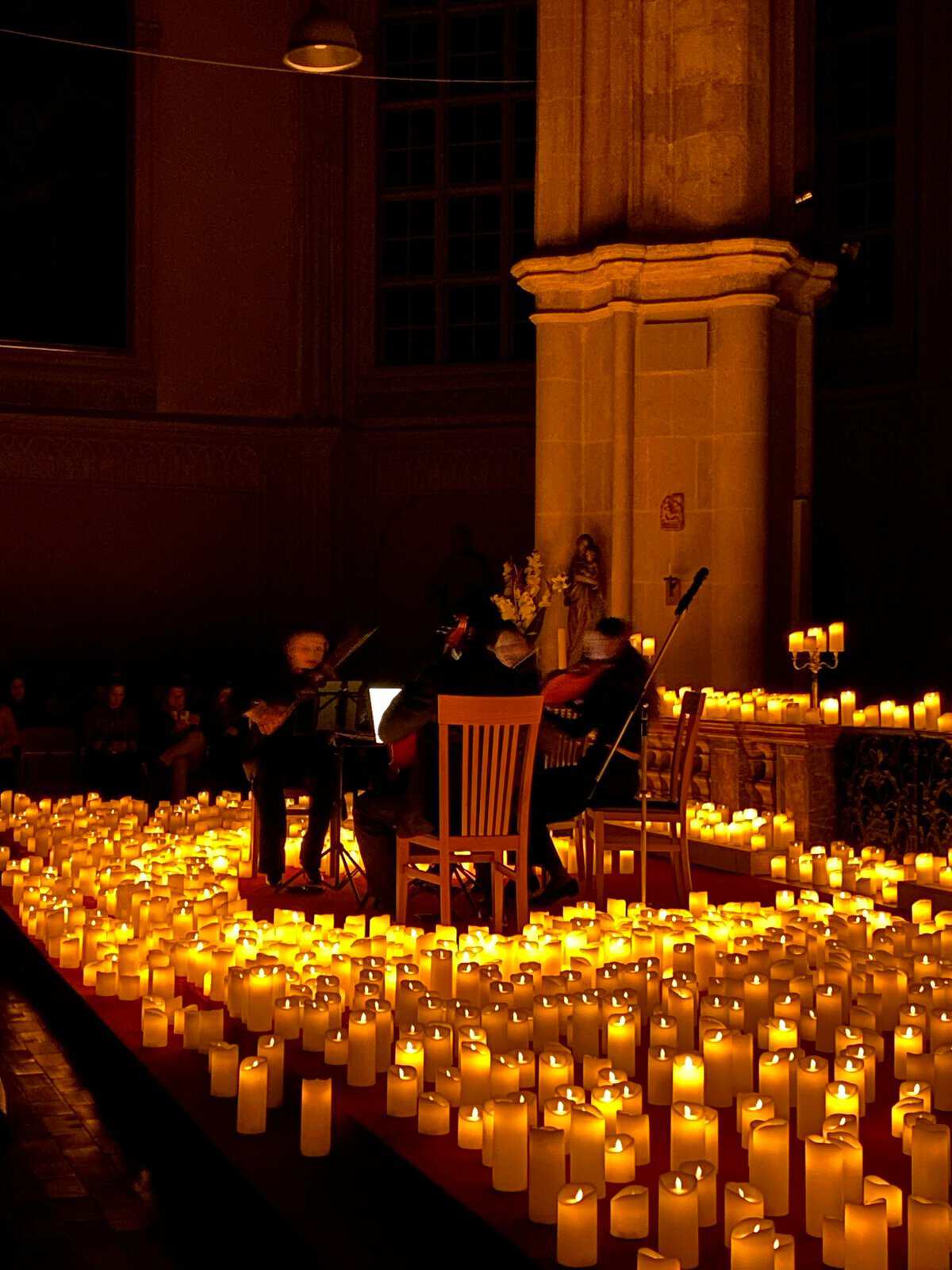 Concierto íntimo con músicos tocando en un escenario rodeado de velas en una catedral de León, Guanajuato, México.