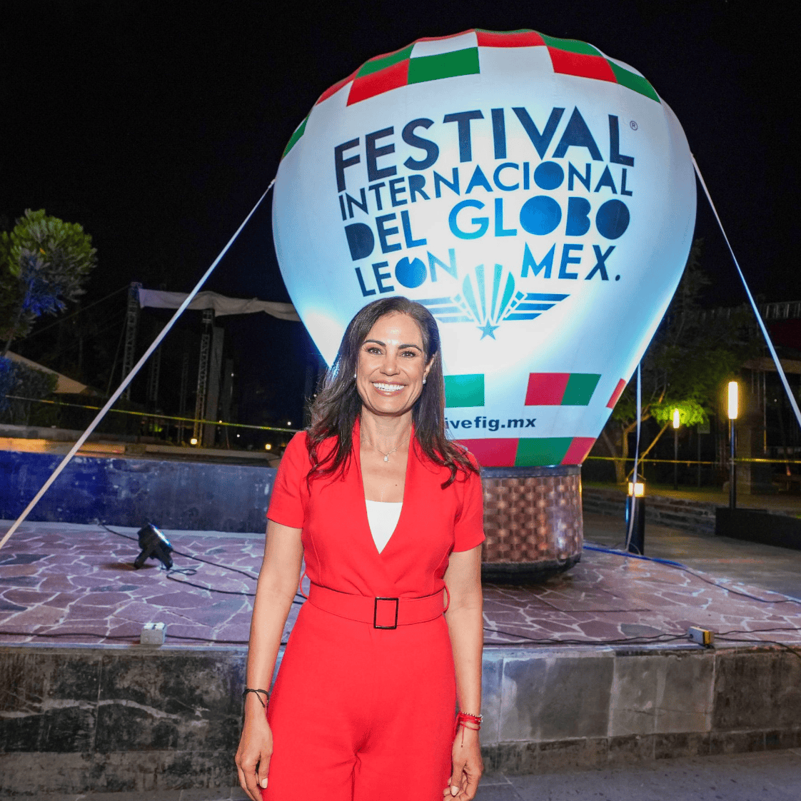 Mujer sonriendo en Festival Internacional del Globo en León, Guanajuato, con globo aerostático en fondo.