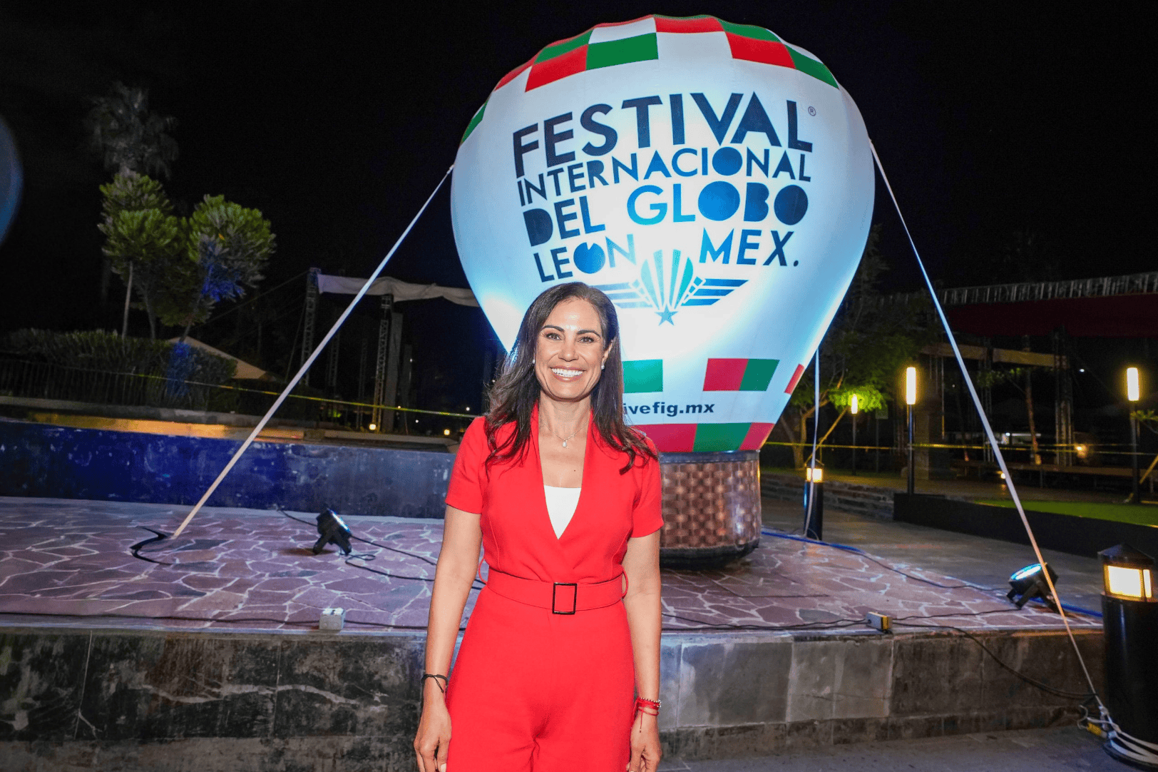 Mujer sonriendo en Festival Internacional del Globo en León, Guanajuato, con globo aerostático en fondo.
