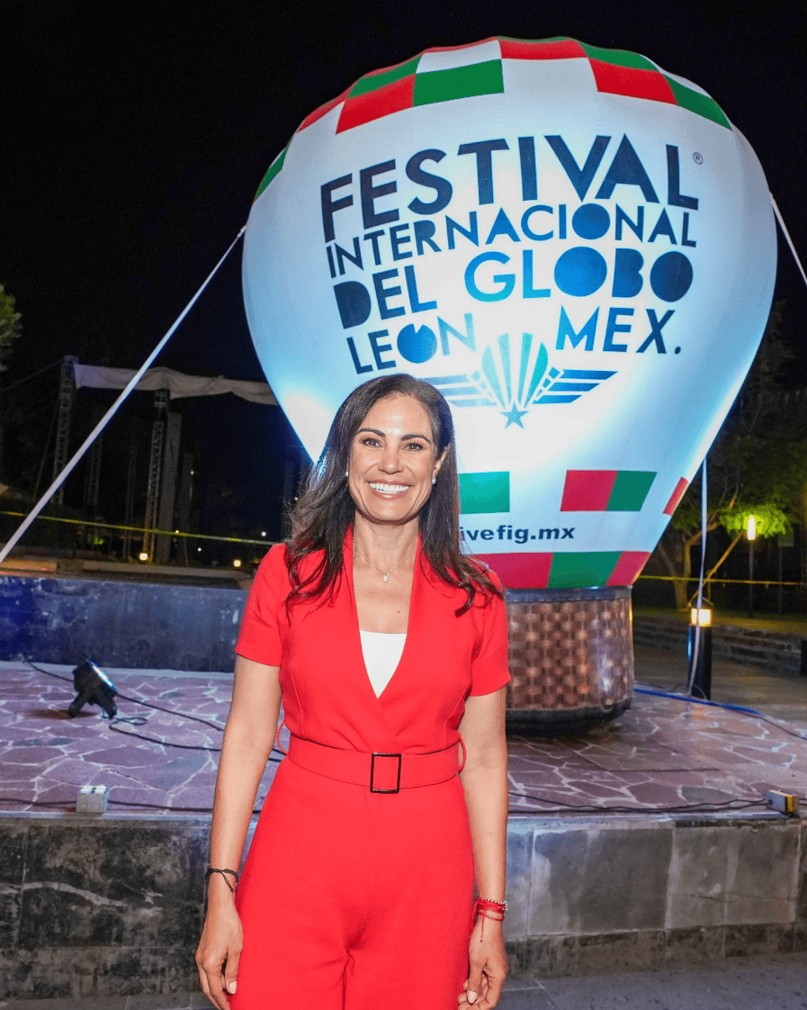 Mujer sonriendo en Festival Internacional del Globo en León, Guanajuato, con globo aerostático en fondo.
