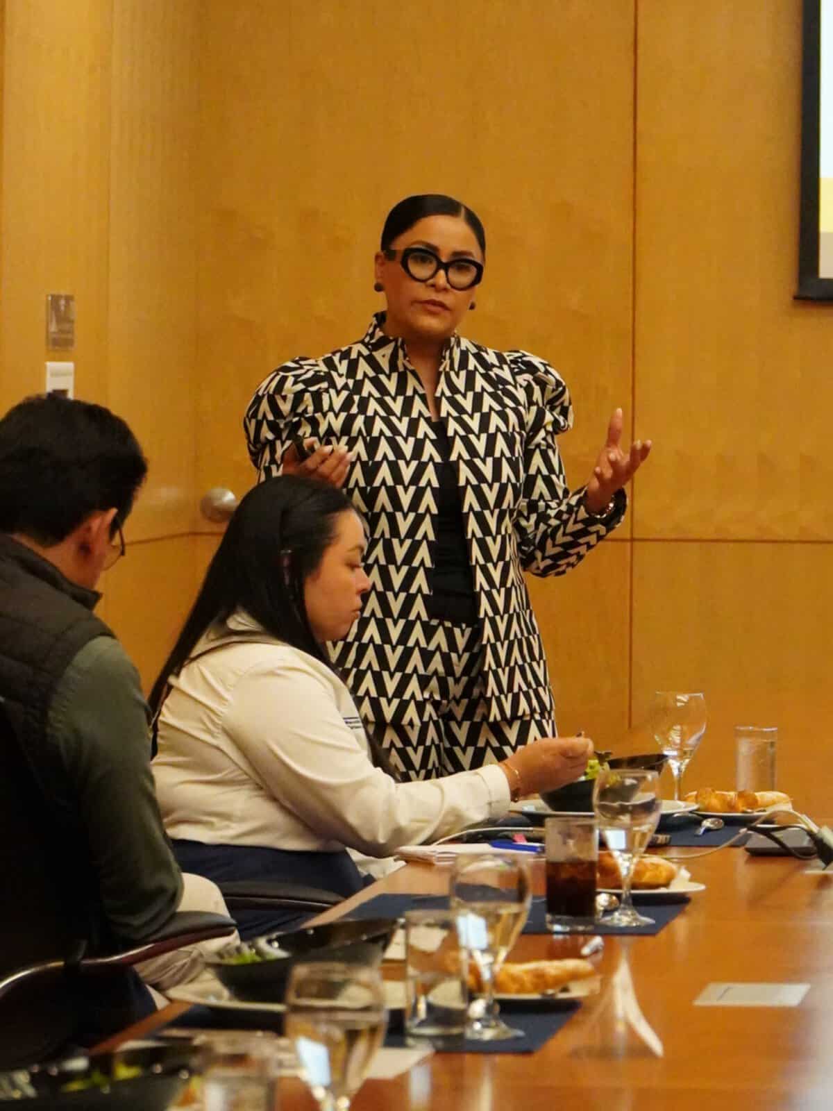 Mujer conferencista en León Guanajuato durante evento, hablando frente a audiencia en sala moderna y elegante.