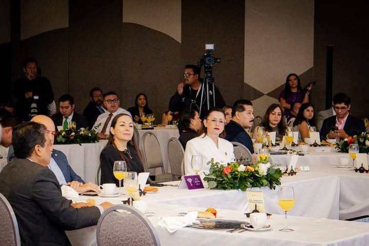 Participantes en conferencia en León, Guanajuato, México, en un evento formal con asistentes atentos y presentadores.