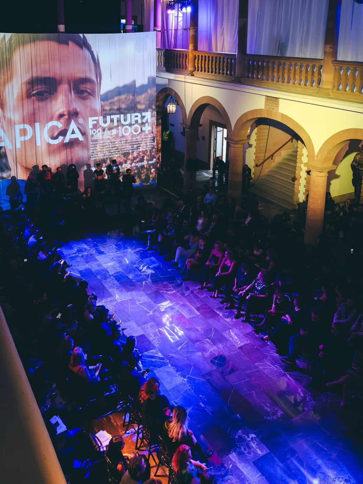 Conferencia en León con gran asistencia, proyección de video y ambiente cultural vibrante en un espacio histórico.