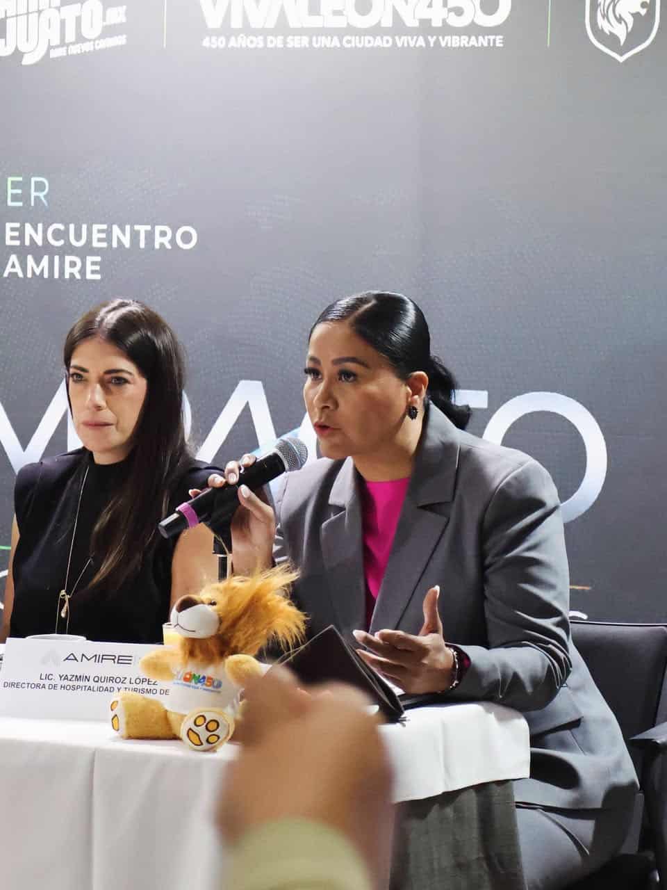 Mujer en conferencia en León, Guanajuato, hablando con micrófono en evento oficial.