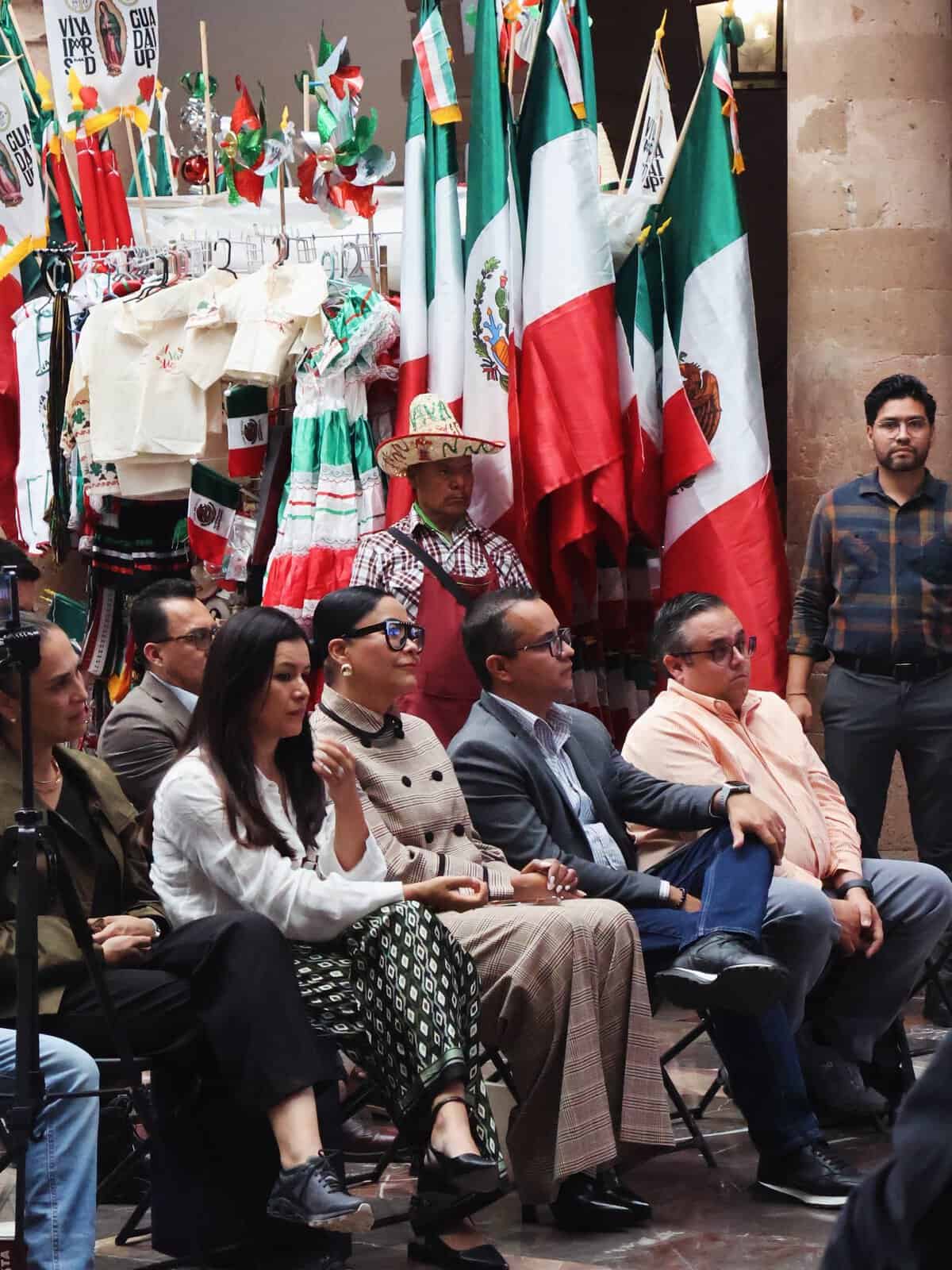 Grupo de personas en evento cultural con banderas mexicanas y artesanías tradicionales en León, Guanajuato.