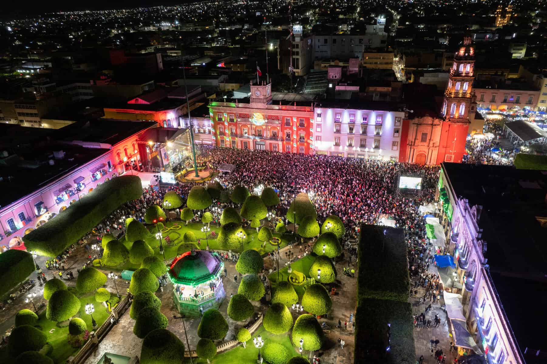 Vista aérea de la celebración en León con luces, música y gran afluencia de público en la plaza principal.