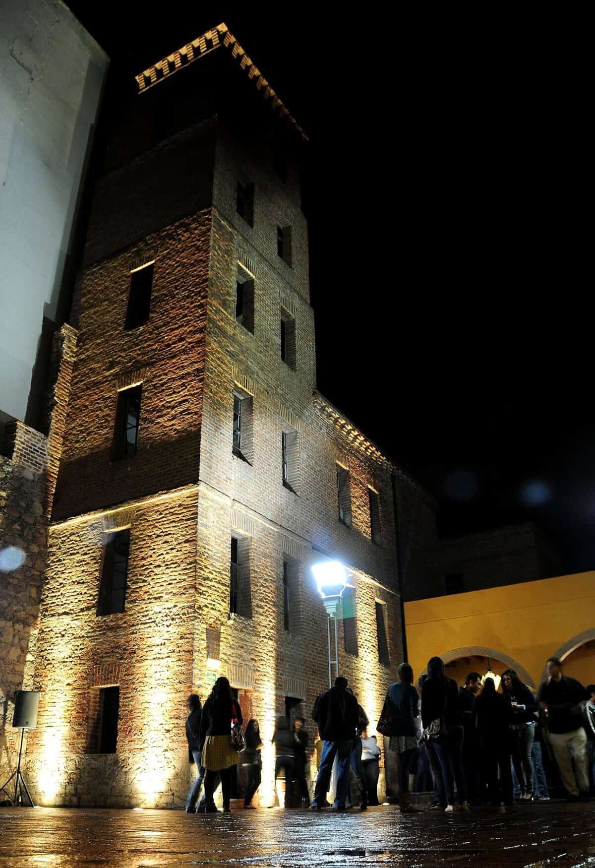 Torre antigua en León iluminada de noche, resaltando su arquitectura y detalles en piedra y ladrillo.