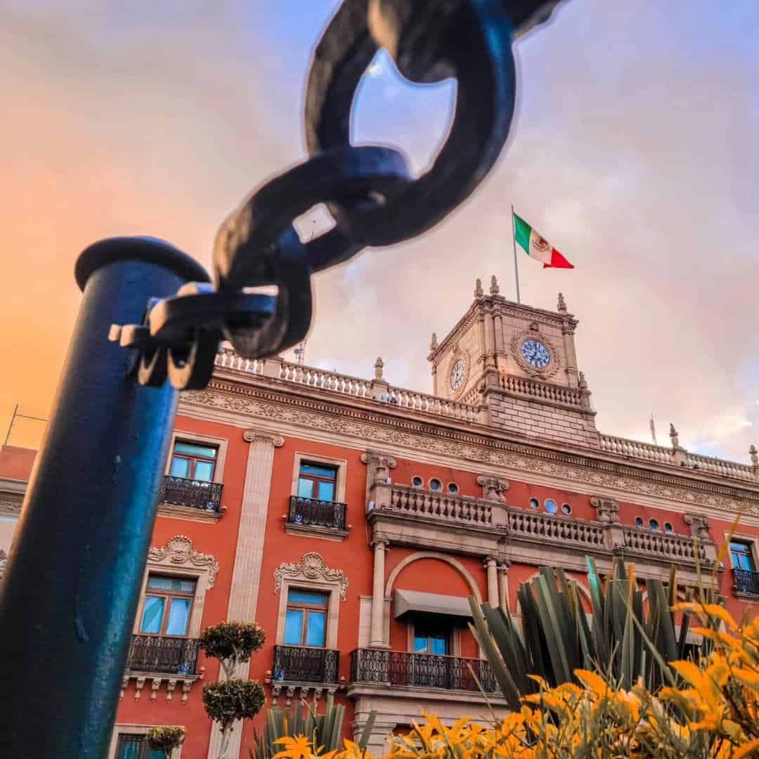 Fachada del edificio histórico en León con detalles arquitectónicos y bandera mexicana en la cima.