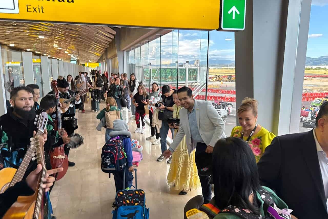 People at León airport with suitcases and live music, waiting for international flights.