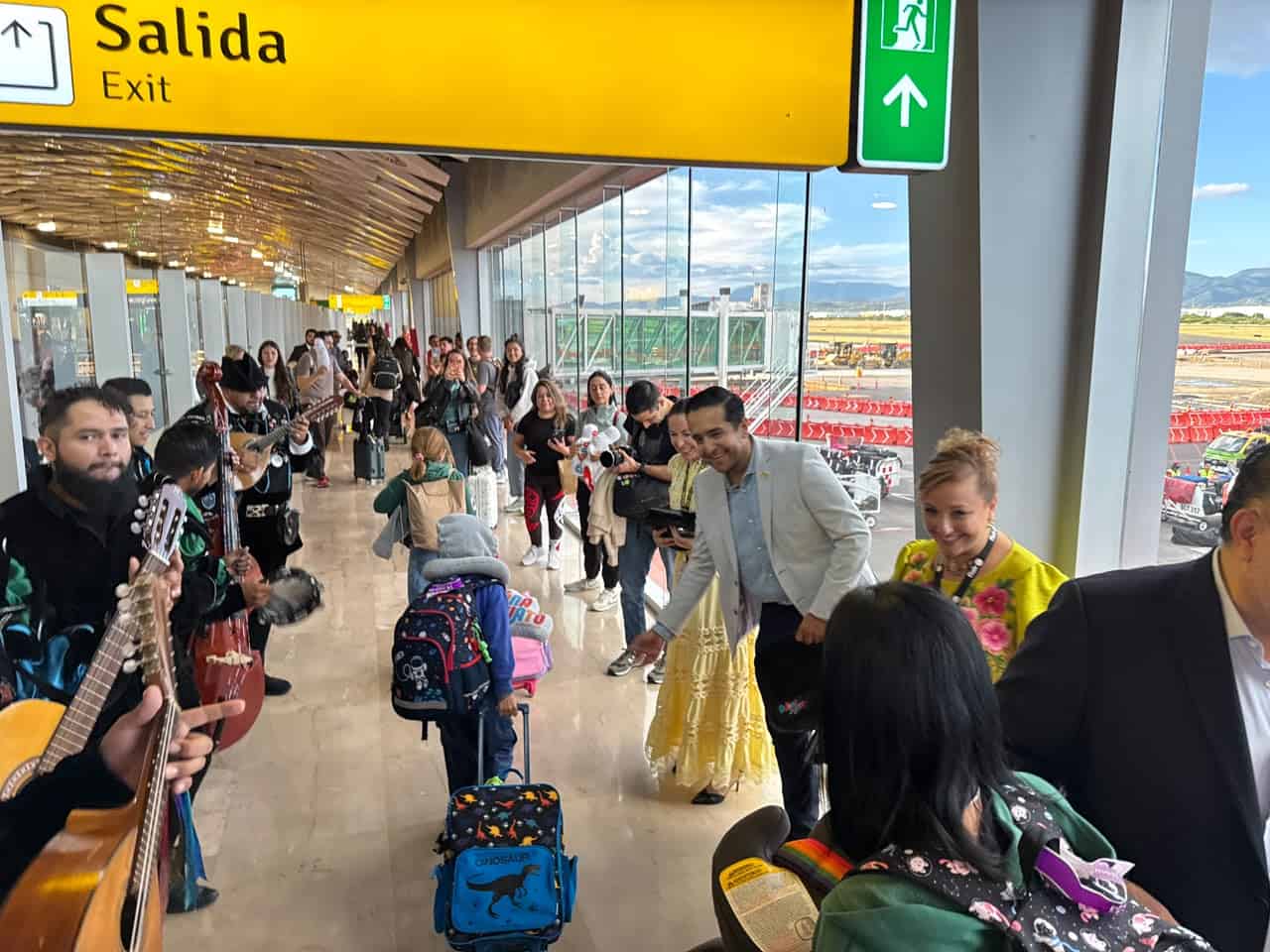 People at León airport with suitcases and live music, waiting for international flights.