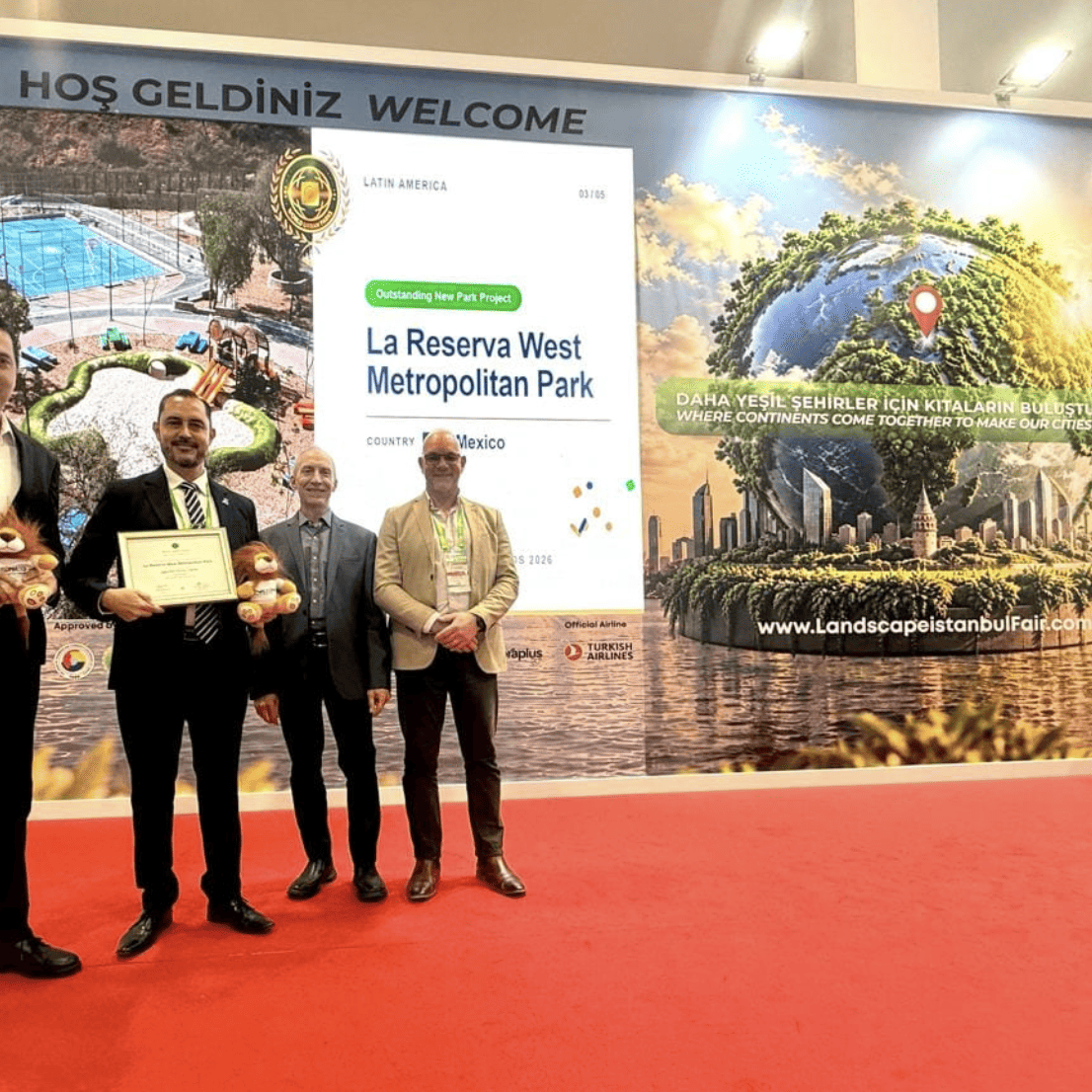 Cuatro personas en evento de premiación en León, Guanajuato, con pantalla que muestra parques y reconocimiento internacional.