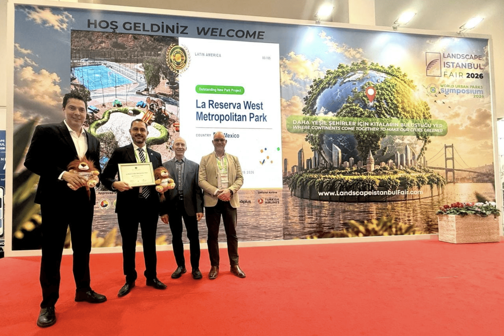 Four people at an award ceremony in León, Guanajuato, with a screen showing parks and international recognition.