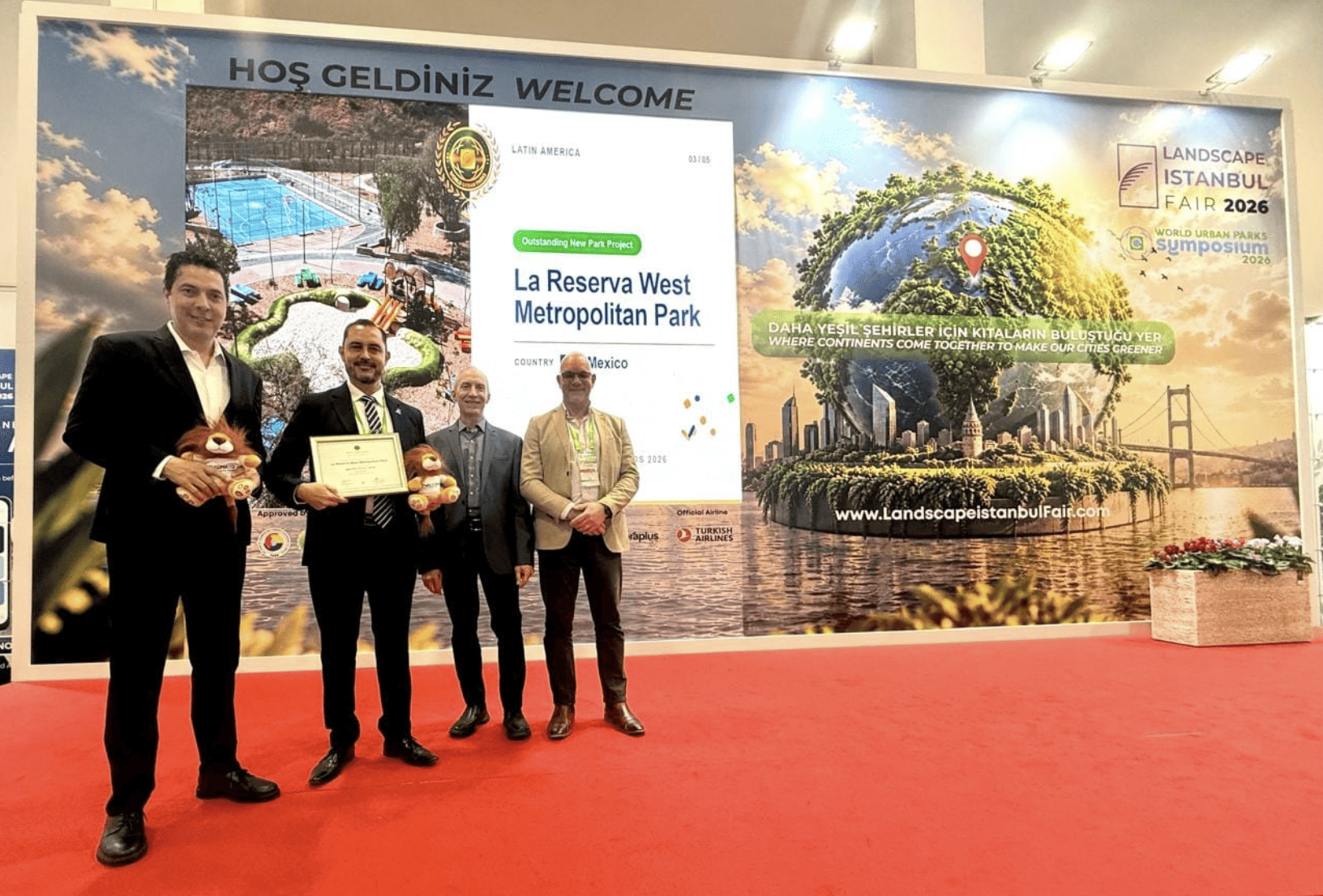 Cuatro personas en evento de premiación en León, Guanajuato, con pantalla que muestra parques y reconocimiento internacional.